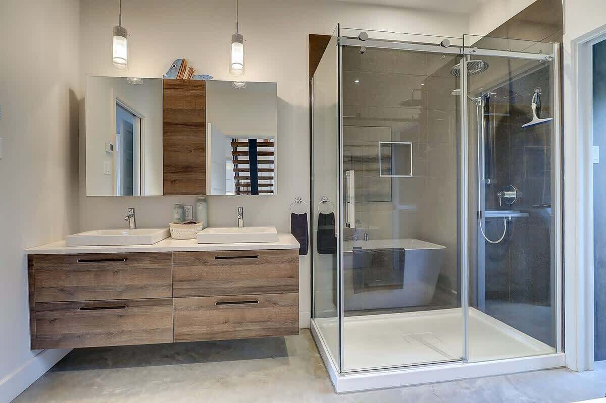 Ein modernes Badezimmer mit zwei Waschbecken, einem großen Spiegel, Holzschränken und einer Duschkabine aus Glas.