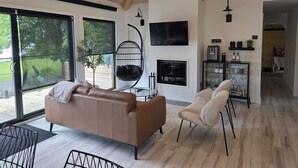 Una sala de estar moderna con un sofá de cuero marrón, un sillón colgante, una chimenea y un televisor montado en la pared.