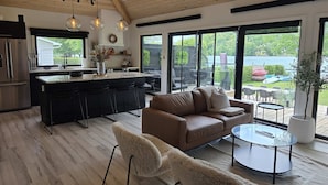 Una cocina moderna con una isla central, un comedor con mesa de vidrio y una sala de estar con sofá y sillones.