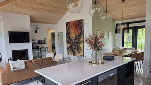 Una cocina moderna con una isla central, un comedor con mesa de madera, una sala de estar con sofá y un cuadro grande en la pared.