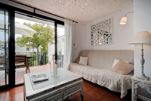 A cozy living room with a sofa, a table with a candle, and a view of the outdoors. - Townhouse, seaview, direct access to beach, sleeps 4, swimming pool!! (Estepona)