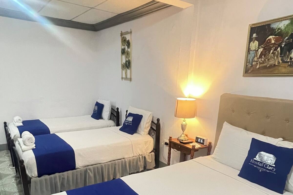 A hotel room with two beds, each with blue and white bedding, a nightstand with a lamp, and a painting on the wall.