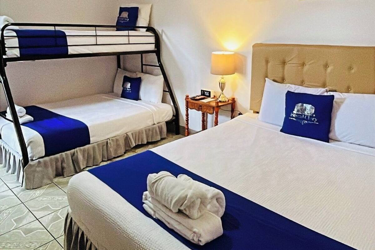 A hotel room with two single beds, a bunk bed, a bedside table with a lamp, and an air conditioning unit.