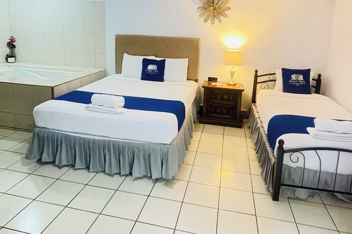A hotel room with two beds, a small bedside table, a nightstand, a wall-mounted flower decoration, and a bathroom with a bathtub.