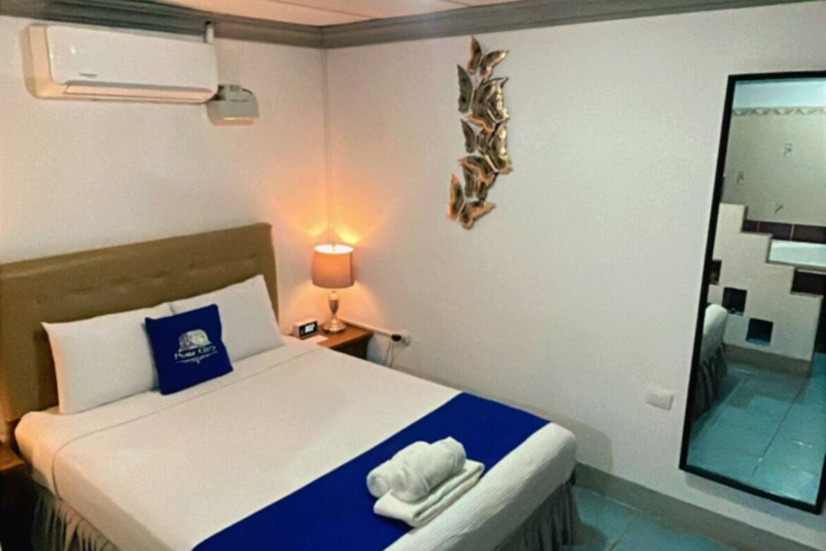 A hotel room with a bed, a bedside lamp, a wall-mounted air conditioner, and a mirror.