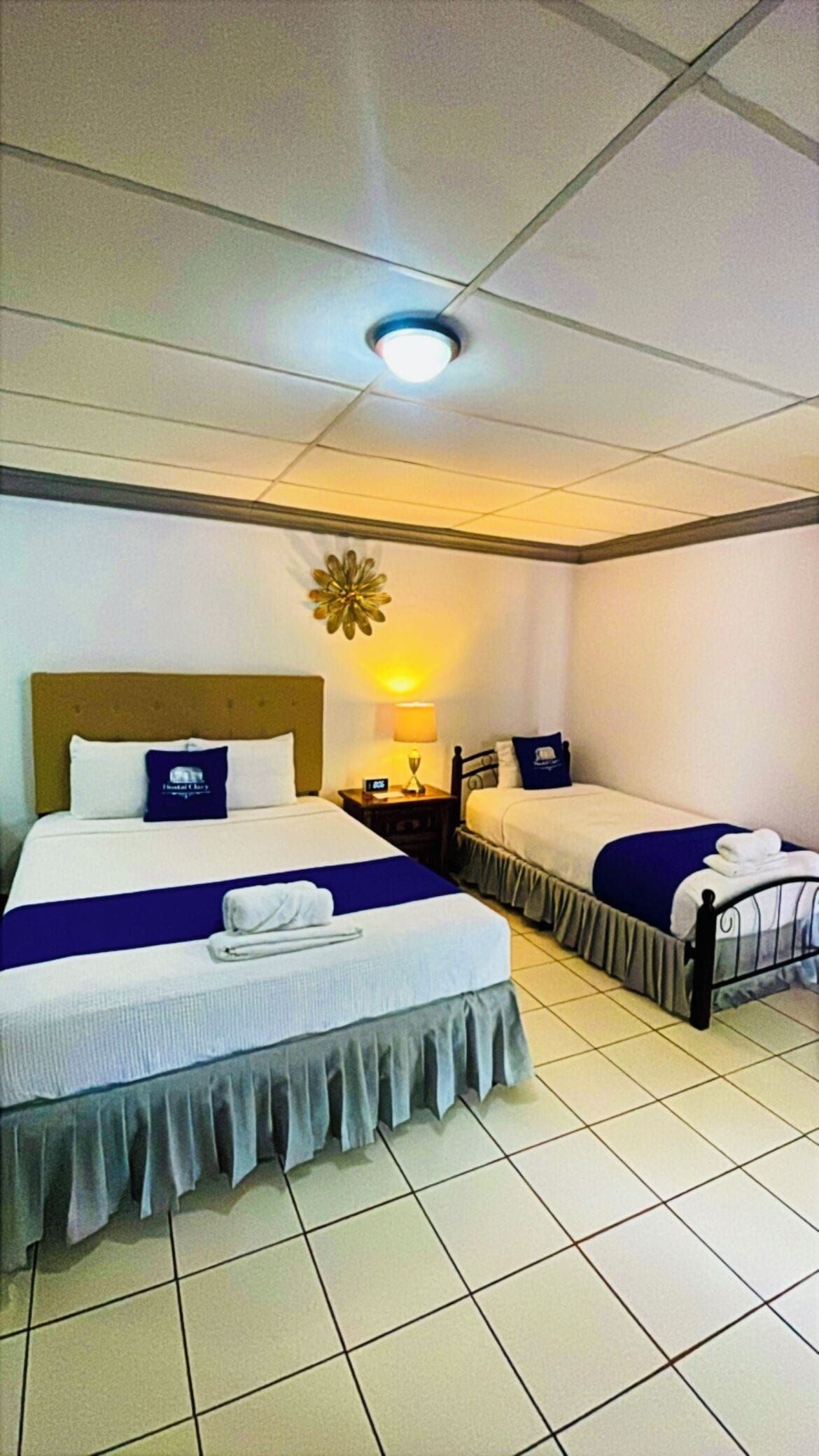 Een hotelkamer met twee bedden, een nachtkastje, een lamp en een plafondlamp.