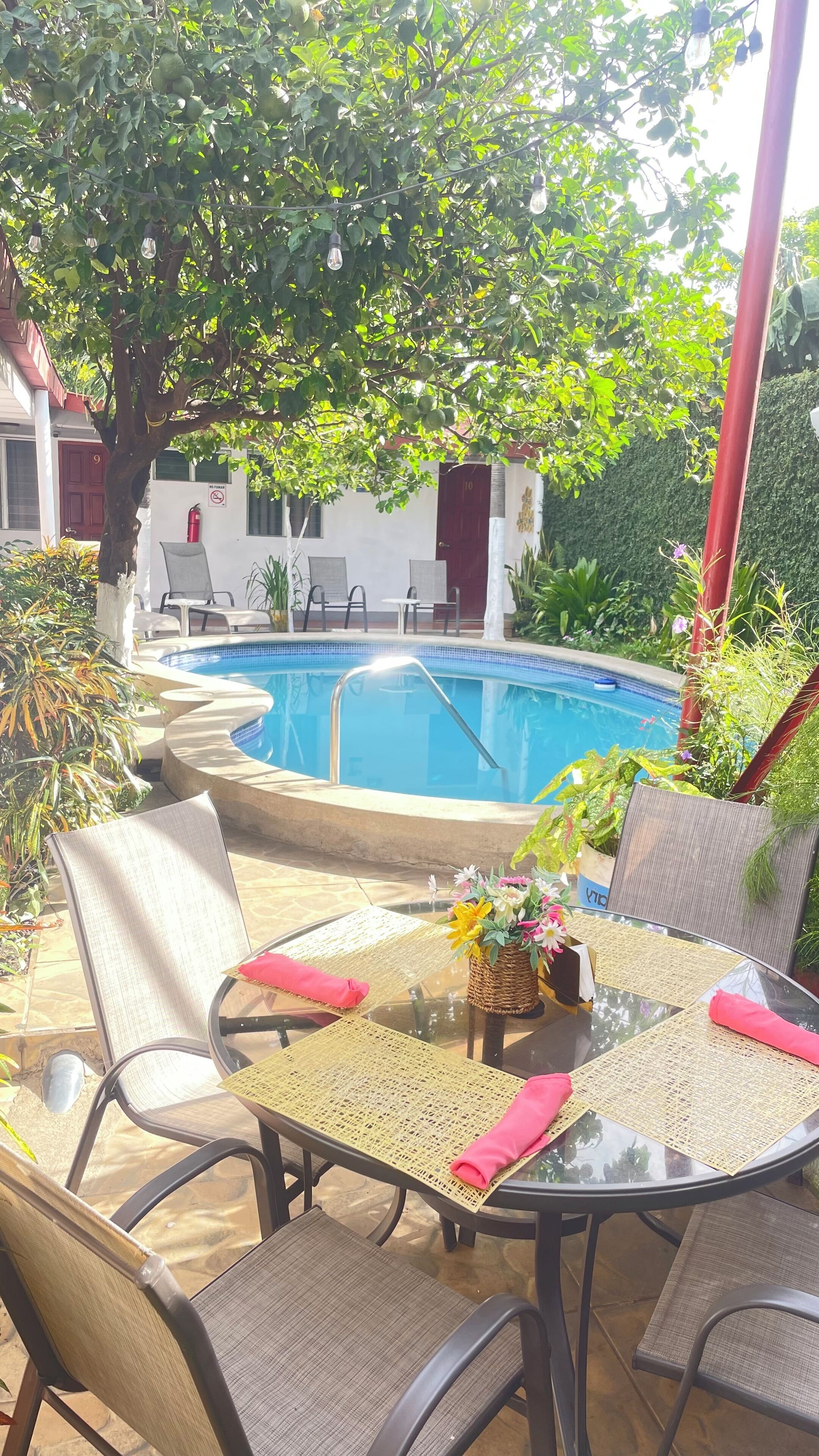 Un área junto a la piscina con una mesa redonda, sillas y una pileta pequeña.