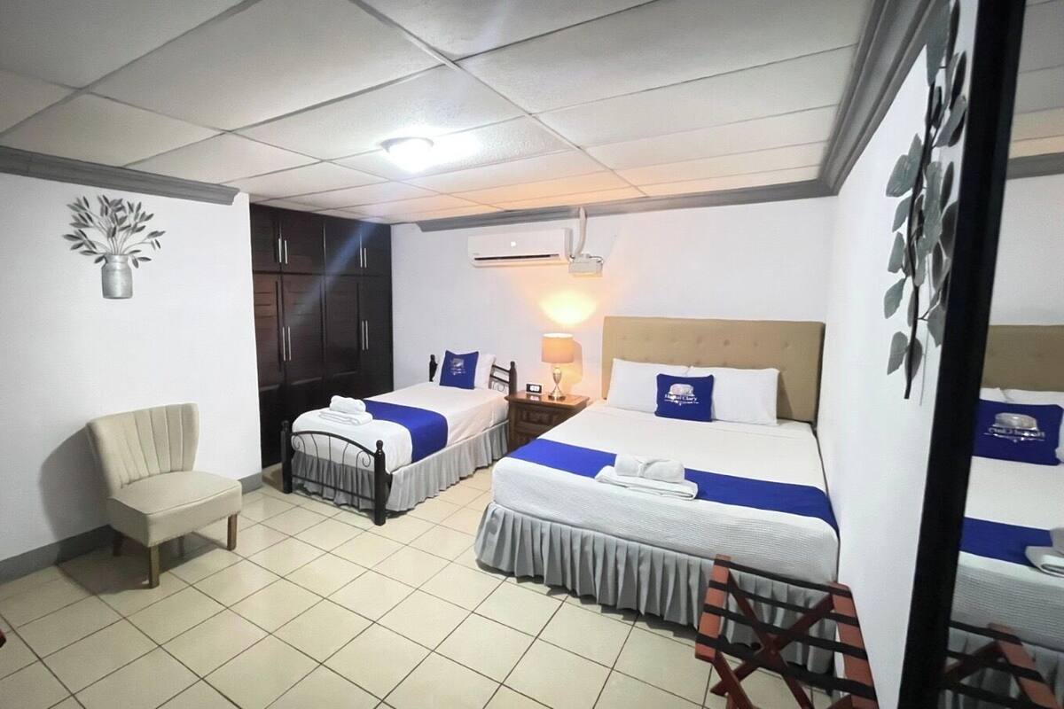 A hotel room with two single beds, a chair, a wardrobe, and a television.