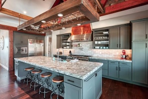 A kitchen with a large island, bar stools, stainless steel appliances, and a brick backsplash. - Luxury 4BR Oasis | Pool & Hot Tub Near Zion (Kanab)