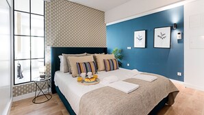 Quarto moderno com cama, almofadas, mesa de cabeceira com abajur e obra de arte na parede.