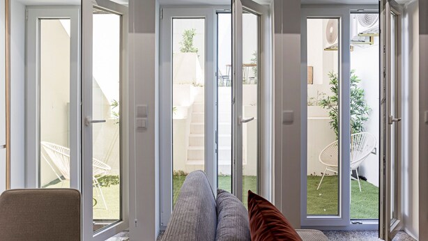 Quarto com porta de vidro deslizante que dá para um pátio com móveis de exterior e um pequeno jardim.