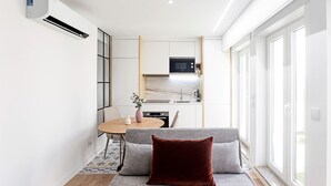 Uma cozinha compacta com eletrodomésticos modernos, uma sala de jantar com mesa e cadeiras, e um sofá com almofada.
