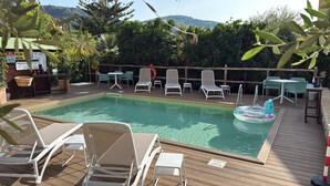 A pool area with lounge chairs and a small table, surrounded by a wooden deck and greenery. - Eterea Charming Suites (Sorrento)
