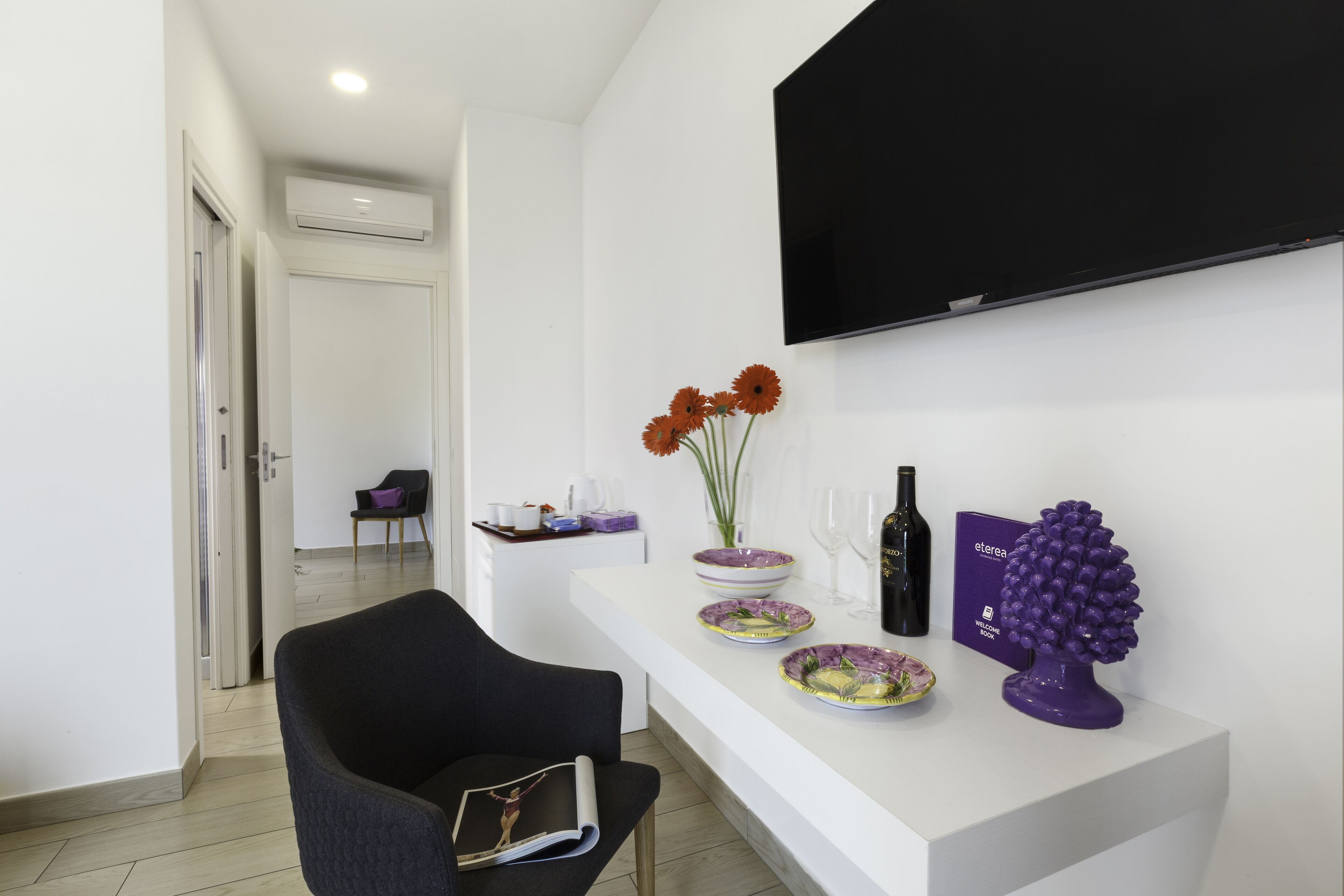 A modern living room with a white console table, a black armchair, and a flat-screen TV mounted on the wall.