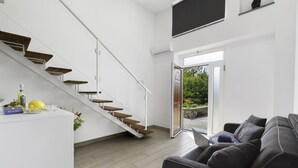 A modern living room with a staircase, a grey sofa, and a small table with a bottle and glasses. - Eterea Charming Suites (Sorrento)