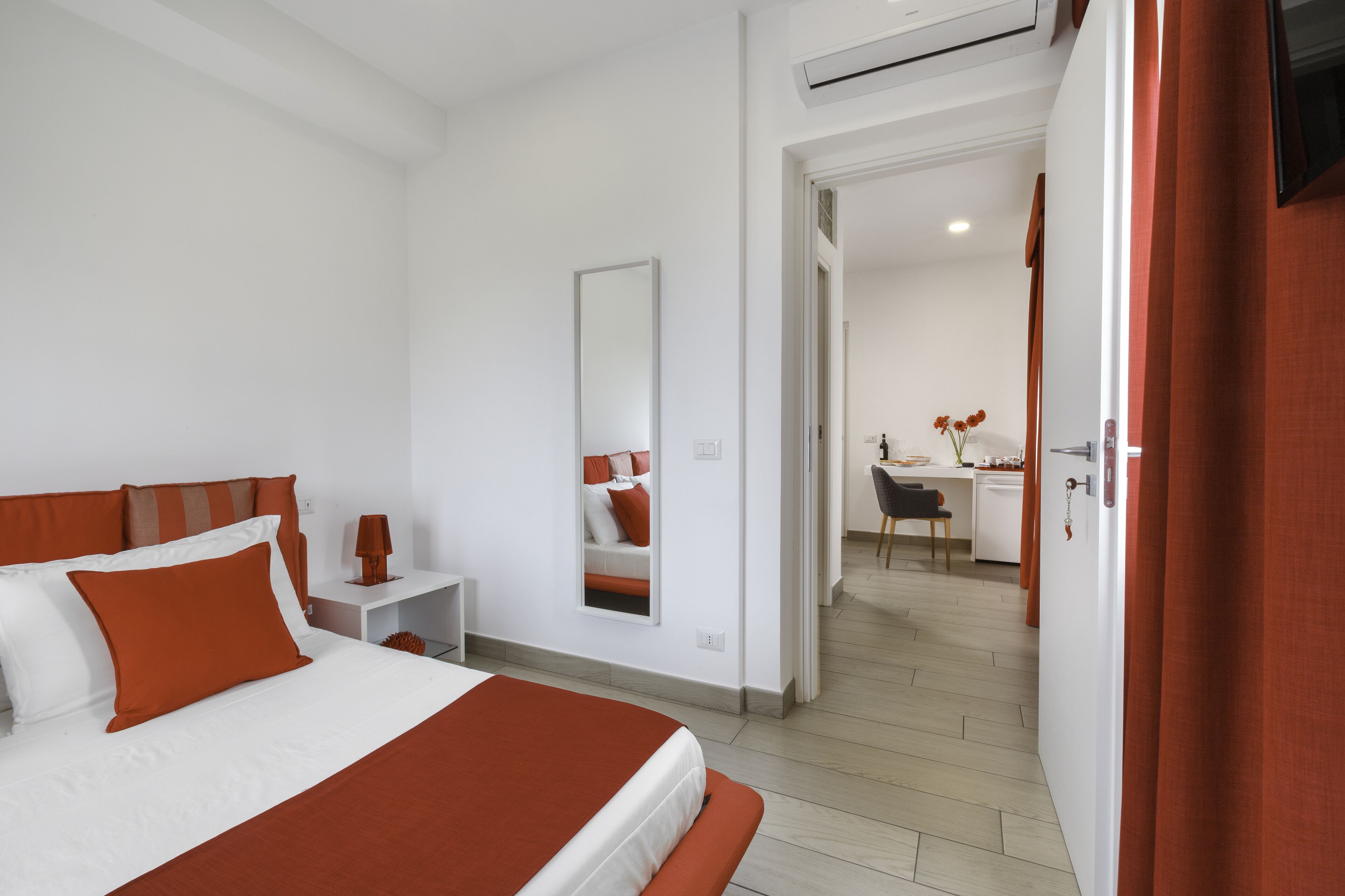 A hotel room with a bed, a desk, a chair, and a mirror.