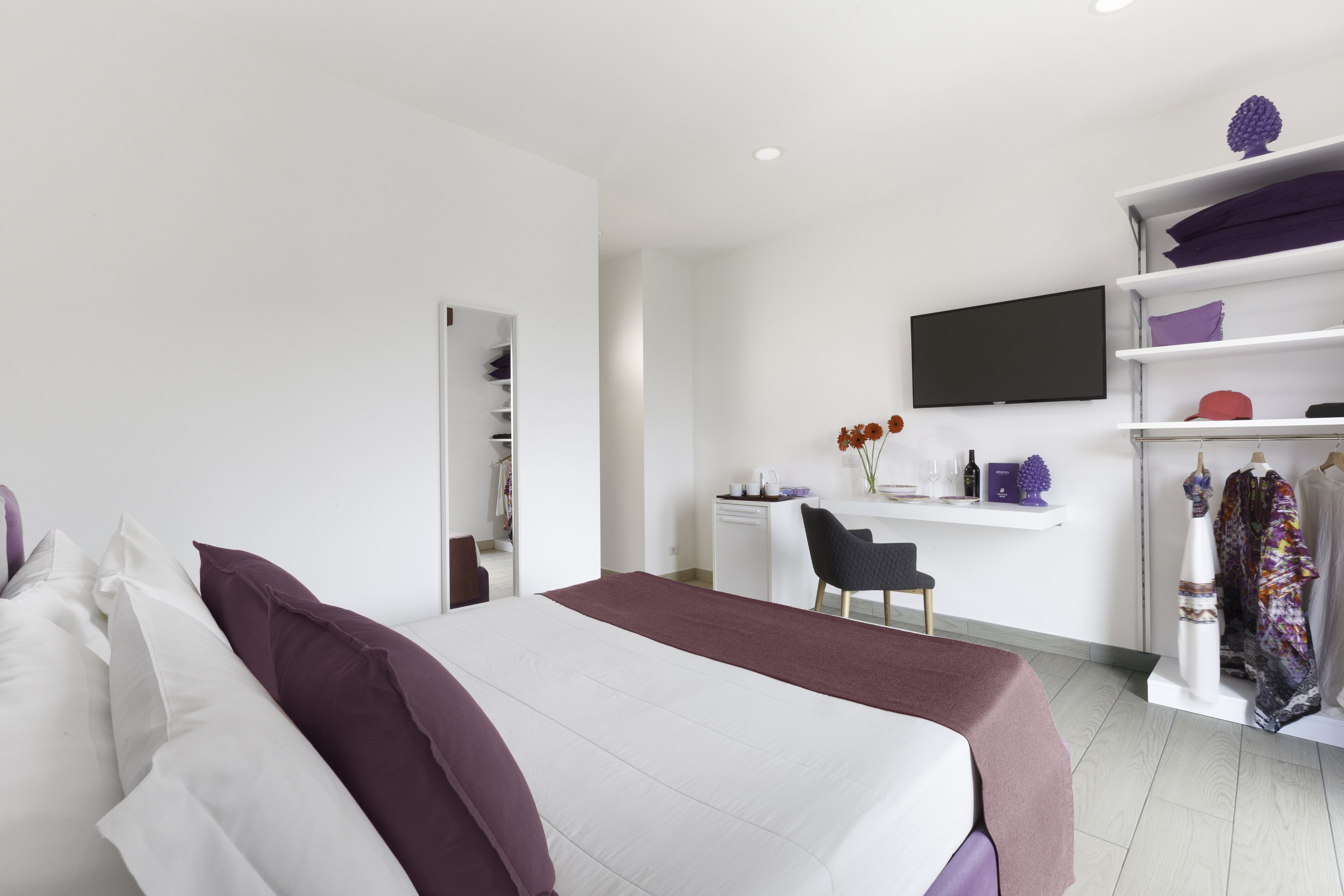 A modern hotel room with a large bed, a desk with a chair, a television, and a wardrobe.