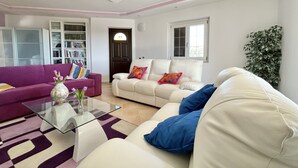 A modern living room with a purple sofa, a white sofa with blue cushions, and a glass coffee table. There is a bookshelf filled with books and a large potted plant. - WE ARE LOCATED IN A VERY EXCLUSIVE AREA, WHO WOULD  KNOW?
 (Sicilia)