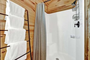 A wooden cabin with a shower area, a towel rack with white towels, and a shower curtain. - RockyRidge Cabin-Amazing Views! (Fredericksburg)