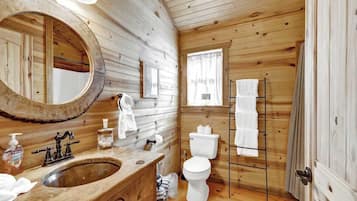 Et badeværelse i en træhytte med en trævask, et stort spejl, et toilet og en håndklæderække.