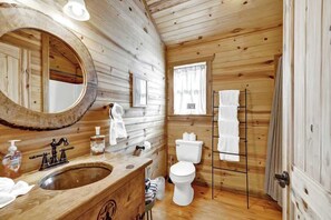 A wooden cabin bathroom with a wooden sink, a large mirror, a toilet, and a towel rack.