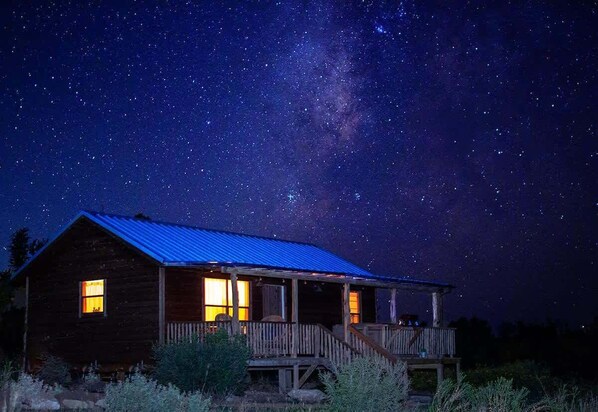A rustic cabin with a porch, under a starry night sky.
