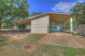 A covered outdoor area with a metal fence, a concrete patio, and a grassy lawn. - Stylish Abode | Minutes to Main St! (Fredericksburg)