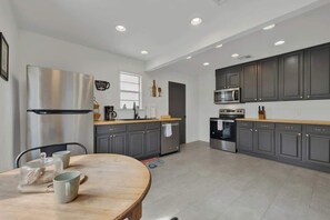 A modern kitchen with grey cabinets, stainless steel appliances, and a wooden dining table with cups. - Stylish Abode | Minutes to Main St! (Fredericksburg)