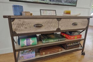 Een houten kast met twee lades en planken, gevuld met gezelschapsspellen, boeken en een blauw decoratief object.