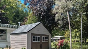 A garden with a small shed, a round table with chairs, and various potted plants. - Quebec Château Richer Côte de Beaupré Canada rent a 4 ½ furnished plus more.... (Chateau-Richer)
