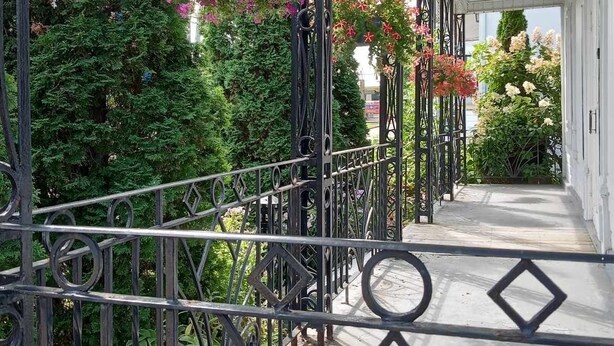 A covered outdoor area with a metal railing, hanging flower baskets, and a pathway leading to a building. - Quebec Château Richer Côte de Beaupré Canada rent a 4 ½ furnished plus more.... (Chateau-Richer)