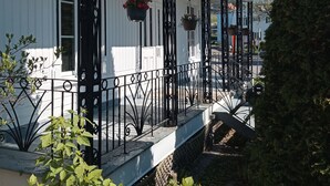 A white building with a porch, black metal railings, and hanging flower baskets. - Quebec Château Richer Côte de Beaupré Canada rent a 4 ½ furnished plus more.... (Chateau-Richer)