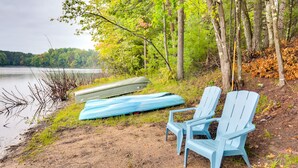 A lakeside scene with a canoe and two Adirondack chairs by the water.