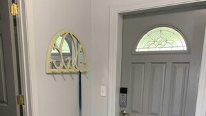A hallway with a grey door, a decorative mirror, a doormat, and a wooden floor.
