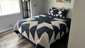 A bedroom with a bed, a nightstand, a lamp, a door, and a window.