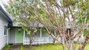 A house with a white picket fence, a green door, and a small tree in the front yard.