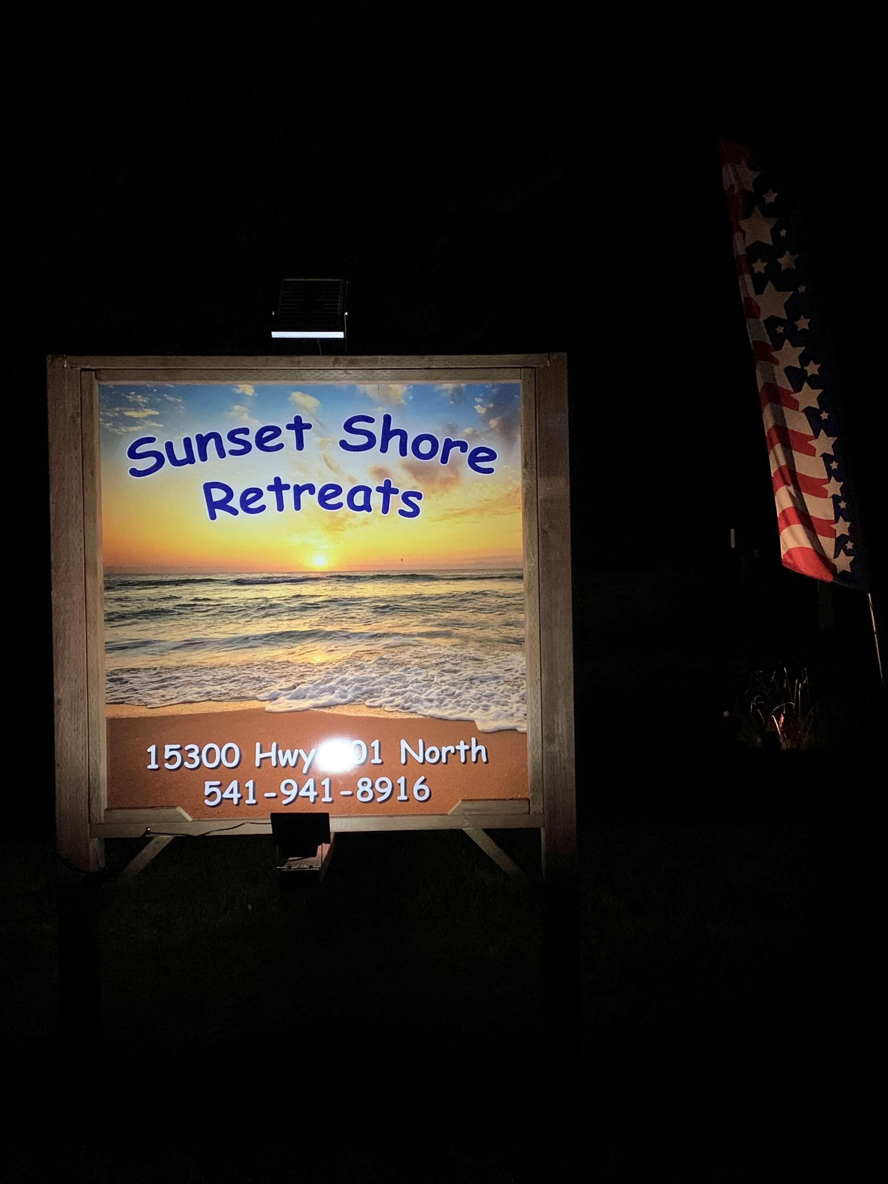 A sign for Sunset Shore Retreats with a sunset view, address, and phone number.