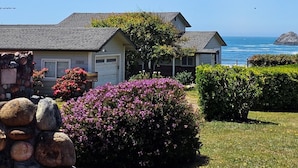 Een huis aan de kust met een garage, een stenen muur en een tuin vol paarse bloemen.