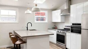 Een moderne keuken met witte kasten, een centraal eiland met barkrukken, een fornuis, oven en een koelkast.