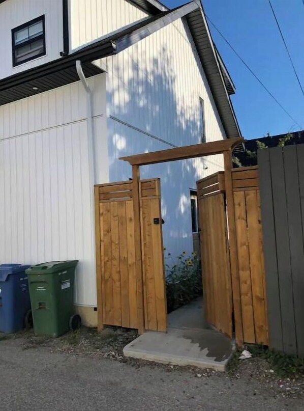 A white building with a wooden gate and two trash bins.