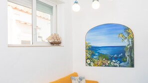 Une pièce avec une fenêtre, un modèle de bateau et un tableau représentant un paysage côtier.