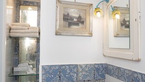 A bathroom with a glass shelf, a framed picture, and a mirror with a light fixture. - VRBO (Anacapri)