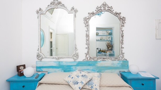 A bedroom with two ornate mirrors, a blue dresser, a bed with a floral pillow, and a shelf with decorative items. - VRBO (Anacapri)