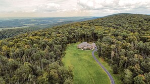 Une grande maison de plain-pied, entourée d’une forêt dense, avec une pelouse bien entretenue et une allée sinueuse.
