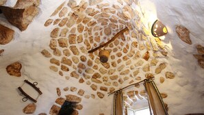 A stone ceiling with a rustic, uneven pattern, a wooden beam, and a hanging light fixture. - Florio house 300 (Santa Maria di Leuca)