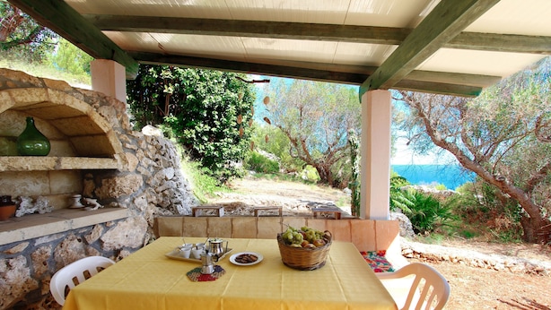 An outdoor dining area with a stone oven, a table with a yellow tablecloth, and a basket of fruit. - Florio house 300 (Santa Maria di Leuca)