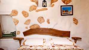 A bed with a wooden headboard, a patterned bedspread, and a wall decorated with rocks and a lantern. - Florio house 300 (Santa Maria di Leuca)