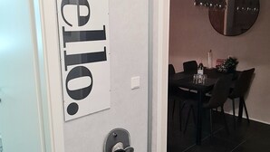 En hall med en skylt med texten ”välkommen”, en skohyll och en matplats med en rund spegel och hängande lampor.