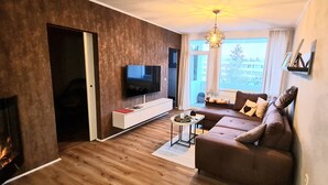 Ett modernt vardagsrum med en platt-TV, en soffa, ett soffbord och en öppen spis.