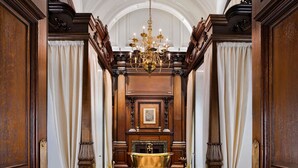 A grand hallway with a chandelier, wooden paneling, and a bathtub. - Raffles London at The OWO (London)